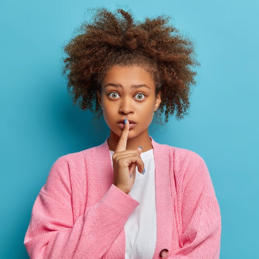 Jeune femme métisse yeux grands ouverts avec l'index sur la bouche sur fond bleu turquoise.
<a href='https://fr.freepik.com/photos/personnes'>Personnes photo créé par wayhomestudio - fr.freepik.com</a>